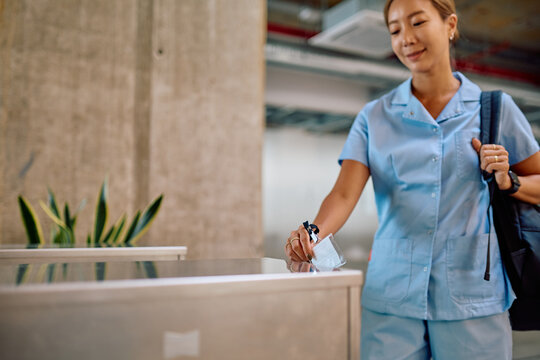 Young female nurse scanning her badge to access an automatic door in a sleek, modern hospital corridor, ensuring secure entry
