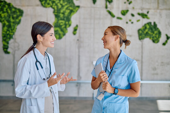 Doctor and nurse having a friendly conversation in a modern hospital, with a world map made of plants in the background, symbolizing global healthcare - Powered by Adobe