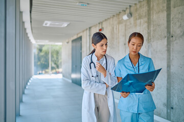Doctor and nurse walking through a hospital hallway, analyzing an x-ray image together while...