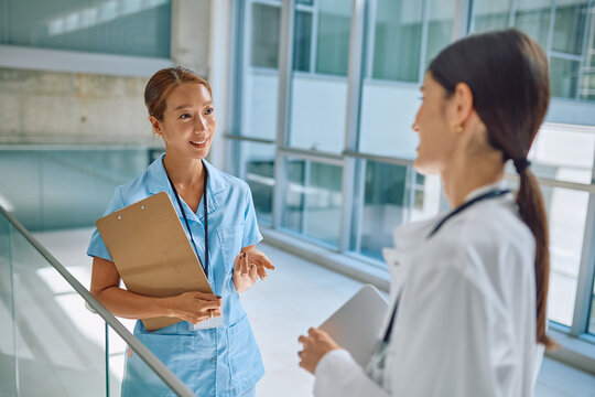 Two healthcare professionals communicate in a modern medical facility, highlighting teamwork and collaboration in a clinical setting - Powered by Adobe