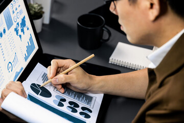 Cropped working asian smart manager with glasses focusing paperwork comparing with business data...