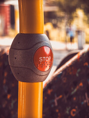 Close-up of a red stop button in a bus, mounted on a yellow pole.