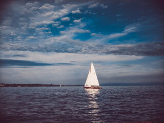 A white sailboat on calm waters under a clear blue sky with delicate clouds – a perfect sailing...
