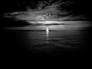Black and white capture of a sailboat at sunset with dramatic light reflections on the water.