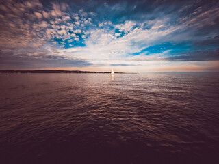 A lone sailboat floats on calm water under a dramatic sky with intense clouds and blue light.