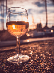 A glass of white wine in the foreground, blurred harbor with sailboats in warm evening light.