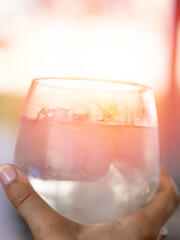 Frosted cocktail glass with pink hue and ice held by hand in warm light