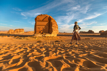Blonde tourist walking in the desert, admiring the monumental Qasr Al Farid, a solitary Nabataean tomb at the UNESCO World Heritage site of Hegra in Al-Ula, Saudi Arabia