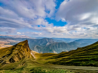 Barren mountain peaks with rocks and a wide view into valleys, sky with dramatic clouds.