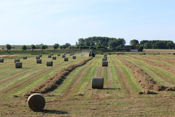 a green field with round bales and a tractor with a baler that makes bales from the rows of hay