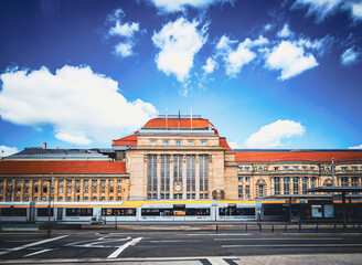 Exterior of a grand train station with red roof and towers under blue sky. Historic atmosphere.