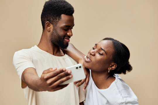 Happy young African couple taking a selfie together against a beige background, showcasing love, joy, and connection in a candid moment - Powered by Adobe