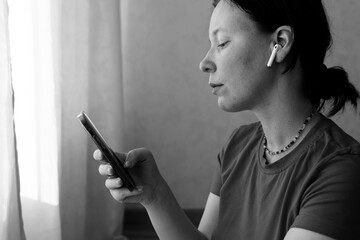Young woman holds smartphone. Acne on face. Black and white photo. Wireless headphones