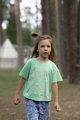 a girl in a light green T-shirt and blue shorts is walking through a forest with pine trees
