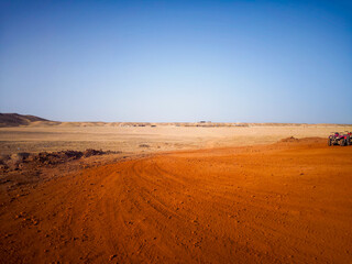 Naklejka premium A red sand path winds through a wide, flat desert – boundless freedom.