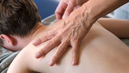 Hands of a masseur are massaging back of a child. A session of therapeutic lymphatic drainage...