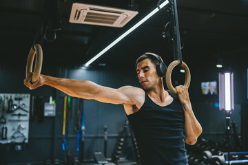 man with headphones do cross fit training on gymnastic rings in the gym