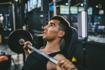 Handsome young athlete man doing bench press workout in gym