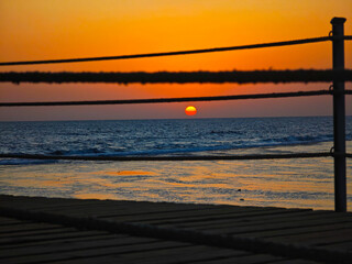 Two stretched ropes frame the setting sun over the sea – graphic and focused.