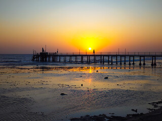 The sky glows golden-orange behind the long pier – a warm and glowing light scene.