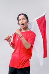 A young Indonesian patriot shouting with pride while holding the national flag, wearing red and...