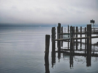 An old wooden dock shrouded in fog at the lake – mysterious and melancholic atmosphere.