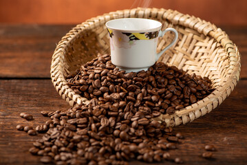 Coffee, beautiful cup of coffee on a heap of coffee beans in a straw sieve, abstract background, selective focus.