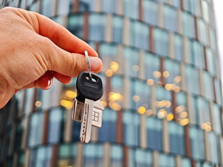 Close-up of hand holding house key and keychain in front of apartment, concept of homeownership