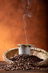 Coffee, beautiful cup of coffee on a heap of coffee beans in a straw sieve, abstract background,...