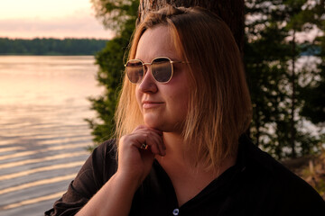 A contemplative woman stands gracefully by the tranquil lake during a stunning sunset