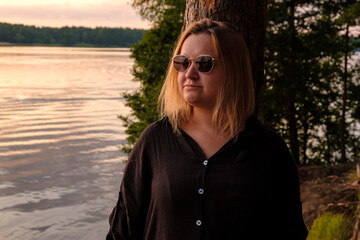 A contemplative woman is enjoying her time by the serene lake during a beautiful sunset