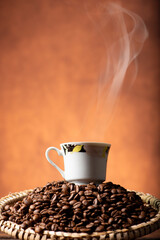 Coffee, beautiful cup of coffee on a heap of coffee beans in a straw sieve, abstract background, selective focus.