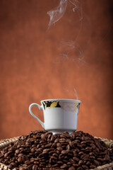 Coffee, beautiful cup of coffee on a heap of coffee beans in a straw sieve, abstract background, selective focus.