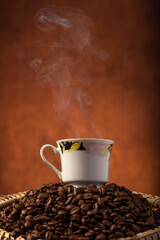 Coffee, beautiful cup of coffee on a heap of coffee beans in a straw sieve, abstract background, selective focus.
