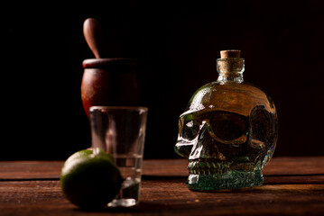 Cachaça from Brazil, bottle of cachaça from Brazil in the shape of a skull, lemon accessories on rustic wood and abstract background, low key photo, selective focus.