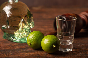 Cachaça from Brazil, bottle of cachaça from Brazil in the shape of a skull, lemon accessories on rustic wood and abstract background, low key photo, selective focus.