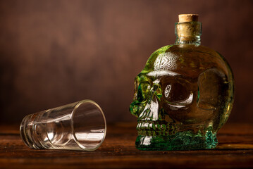 Cachaça, Brazilian cachaça bottle in the shape of a skull and a glass, on rustic wood and abstract background, low key photo, selective focus.
