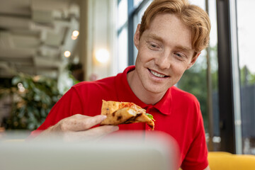 Young ginger man eating pizza and looking enjoyed