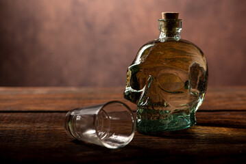 Cachaça, Brazilian cachaça bottle in the shape of a skull and a glass, on rustic wood and abstract background, low key photo, selective focus.