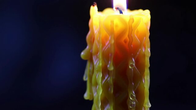 Close-up of a burning candle with flowing yellow wax drips.