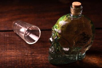 Cachaça, Brazilian cachaça bottle in the shape of a skull and a glass, on rustic wood and abstract background, low key photo, selective focus.