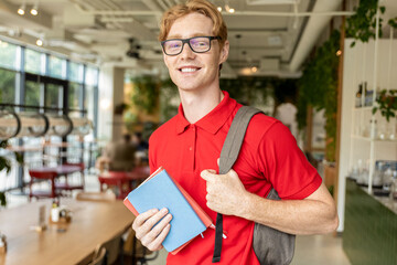 Smiling young guy with books in hands looking positive and joyful