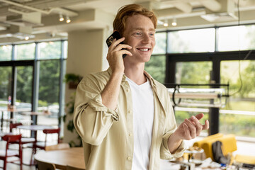 Ginger young man in cafe talking on the phone and looking enjoyed