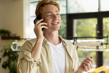Ginger young man in cafe talking on the phone and looking enjoyed