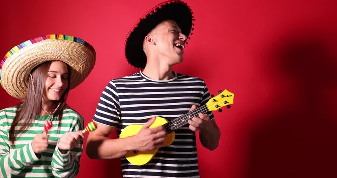 Happy couple in sombrero and Flamenco hats playing musical instruments on red background