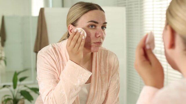 Woman with acne problem cleaning her face near mirror indoors