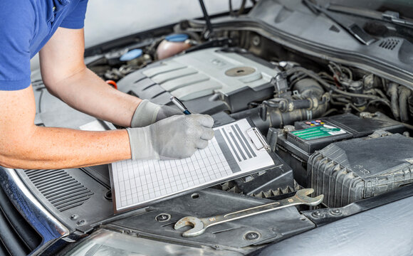 Mechanic writing car repair and maintenance estimate with clipboard in auto workshop.