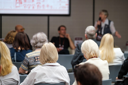 Attentive audience members focus on a speaker presenting at a professional conference or seminar.