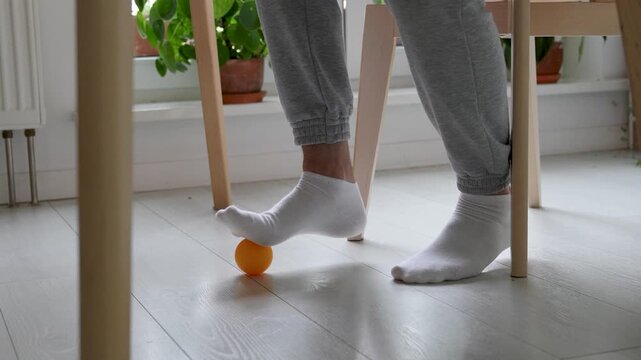 Socked feet rolling orthopedic ball to improve balance and foot mobility on floor. Flat feet correction, balance training, foot muscle activation, arch support, rehabilitation of motor skills