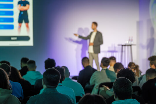 Professional speaker delivering presentation to engaged audience at modern conference event venue.